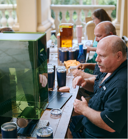Our owner/operator Eric sitting at a table in front of our portable laser, getting ready to engrave custom names onto insulated tumblers at an upscale event at the Ritz in Naples Florida.